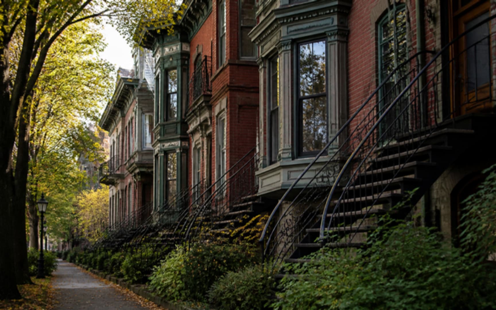 Maisons en rangée de style victorien en brique avec corniches ornementées et escaliers extérieurs en spirale en fer forgé, ruelle verte et feuilles d'automne — illustration générée par IA